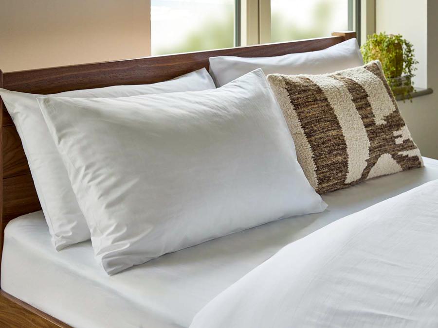 Two soft, white goosedown pillows and soft white duvet on a solid walnut wood bed