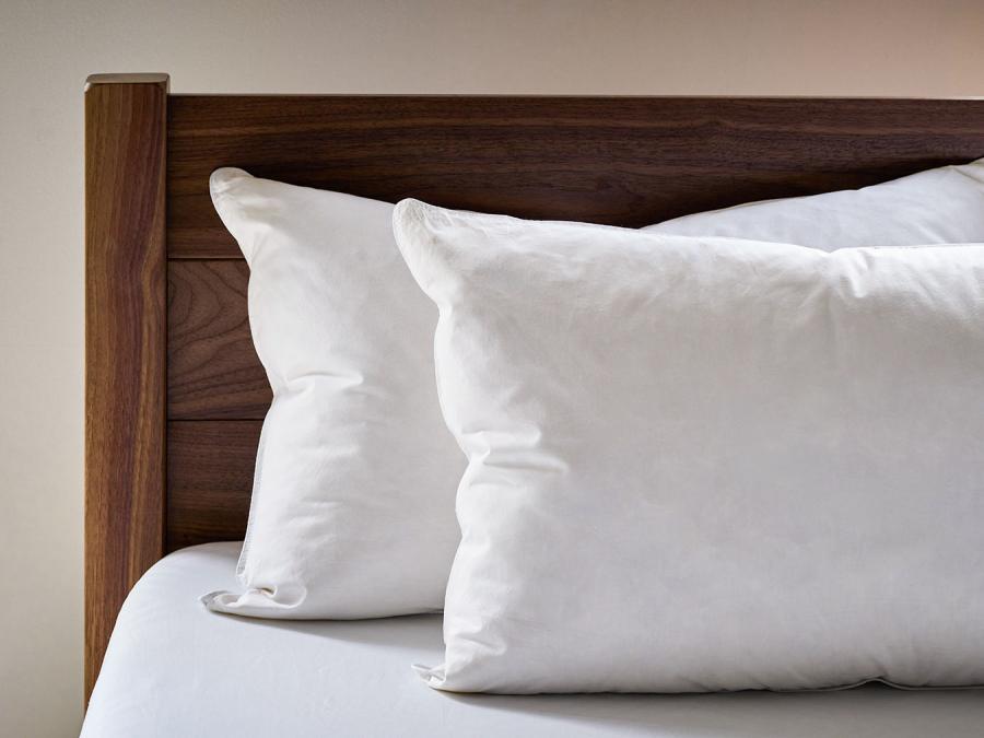 Two goose down pillows next to a solid walnut bed headboard