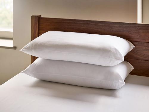 Two hollowfiber pillows on-top of a solid wood bed
