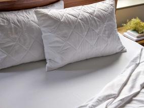 Two pinsonic pillow protectors on pillows on-top of crisp white fitted bed sheet