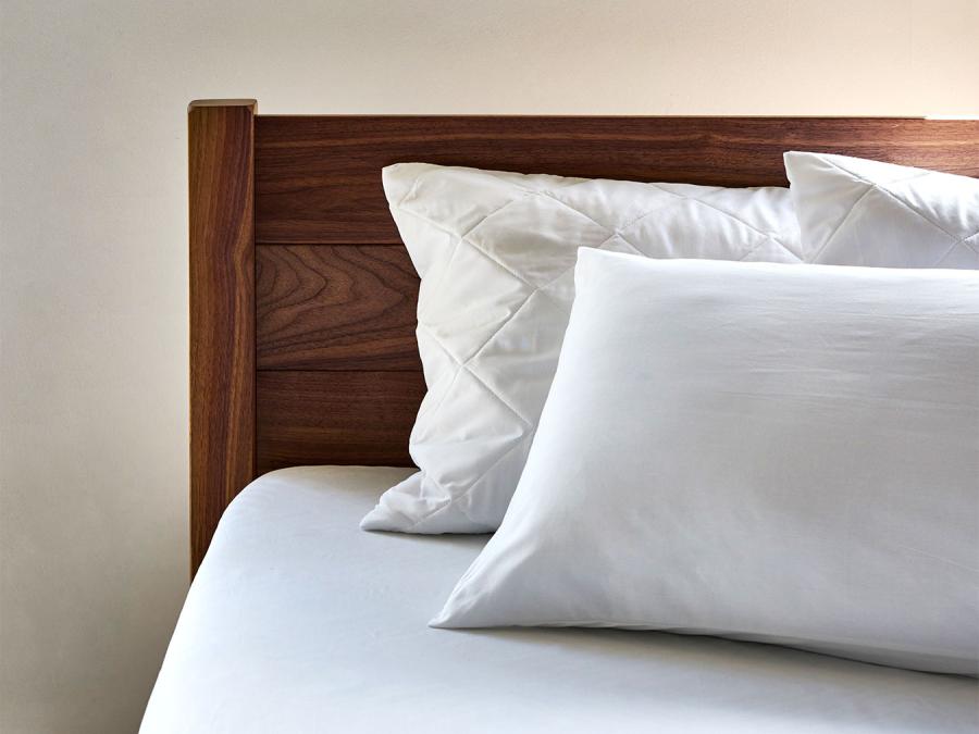 mixture of hollowfiber and goosedown pillows with pillowcase and pinsonic pillow protectors on against a solid walnut wood headboard